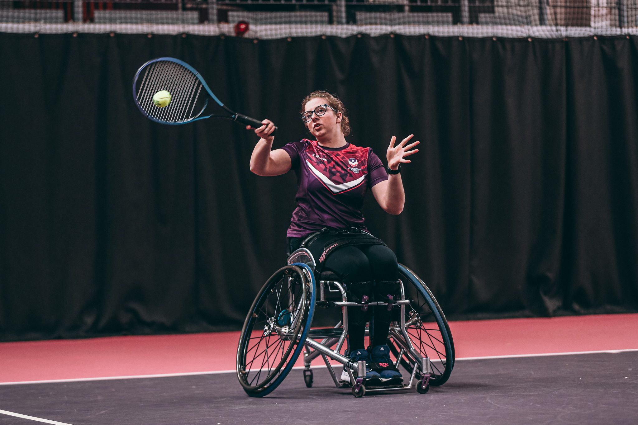 A female wheelchair tennis player on an indoor court